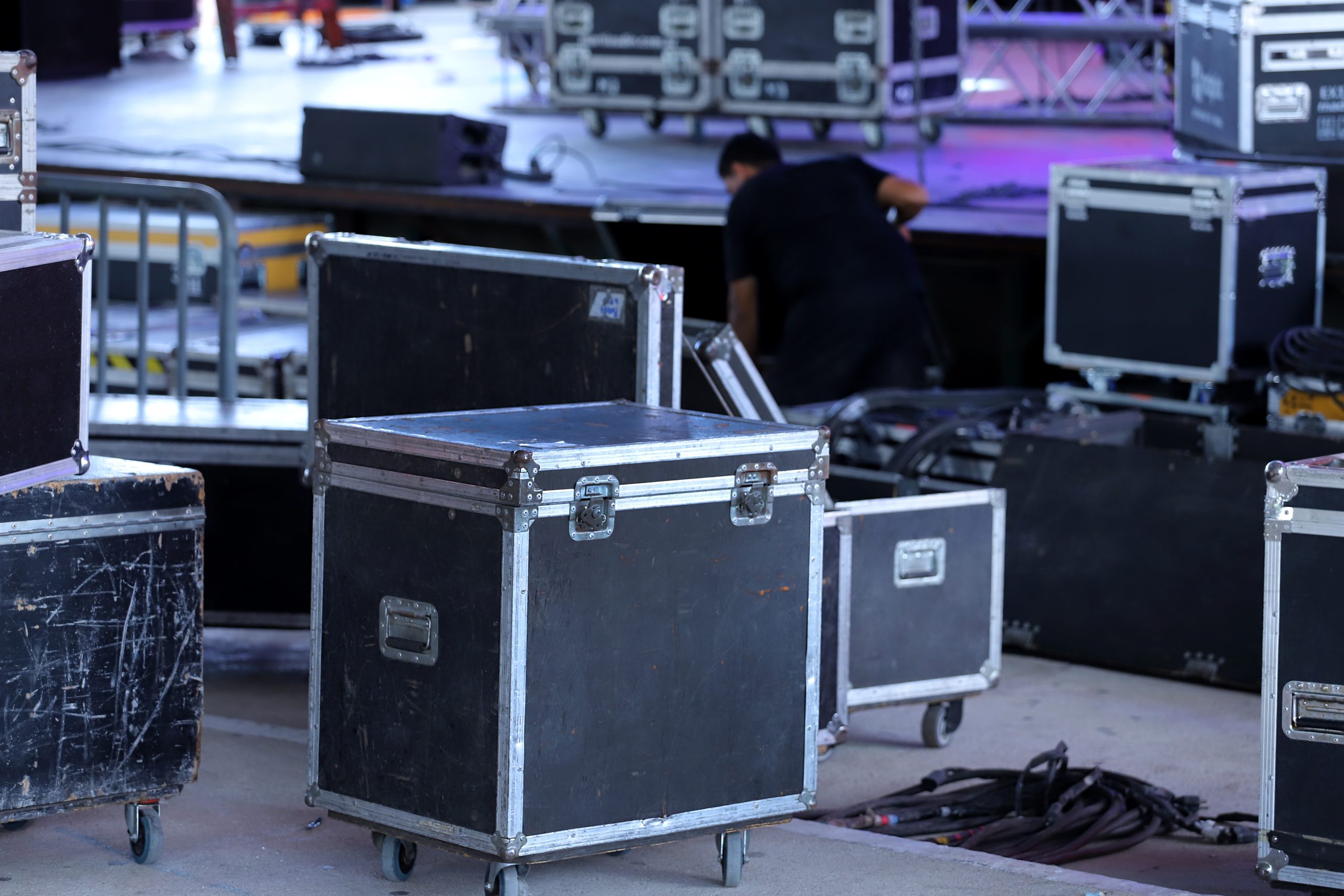 A rack-mounted audio equipment unit sits powered and connected with cables, feeding nearby speakers, on a lit stage with LED panels and colored neon lighting.